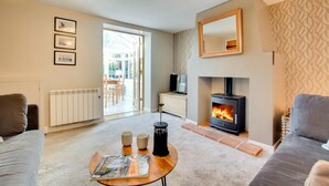 Un salon chaleureux avec une cheminée, un canapé, une table basse avec un magazine, et une vue sur l’extérieur grâce à une porte vitrée.