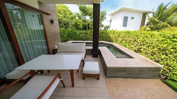 An outdoor patio with a dining table and benches, a small pool, and a modern house in the background.