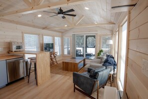 A spacious living area with a wooden ceiling, a sofa, a coffee table, and a television. - Pine Marten Cabin (Pittsburg)