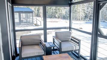 Un espace extérieur abrité, aménagé avec deux chaises et une table, offrant une vue sur un paysage enneigé.