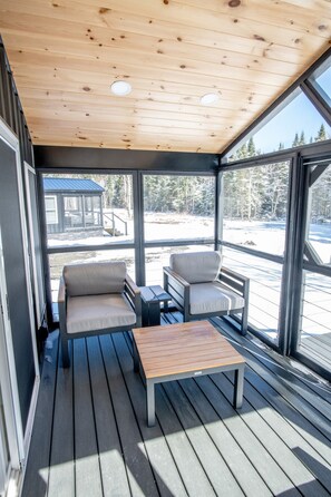 A covered outdoor seating area with two chairs and a table, overlooking a snowy landscape. - Pine Marten Cabin (Pittsburg)
