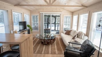 A cozy living room with a wooden ceiling, a glass coffee table, a sofa, and a TV.