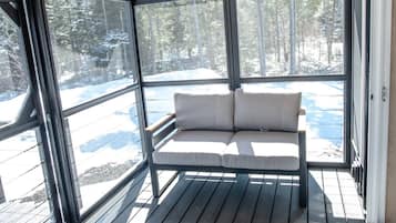 A covered outdoor seating area with a bench and a table, large windows, and a view of a snowy landscape.