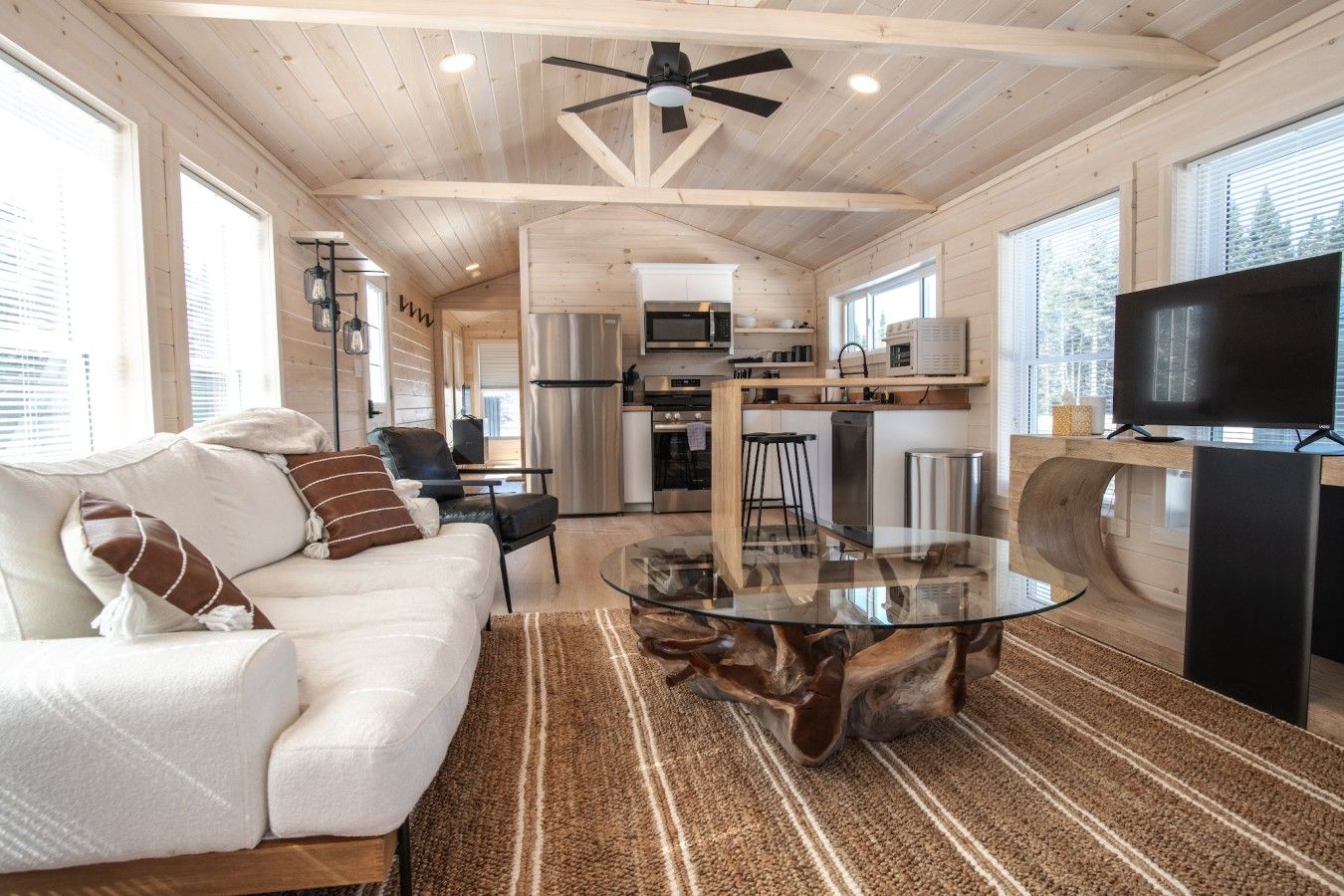 A modern interior with a glass coffee table, white sofa, and a kitchen area with appliances.