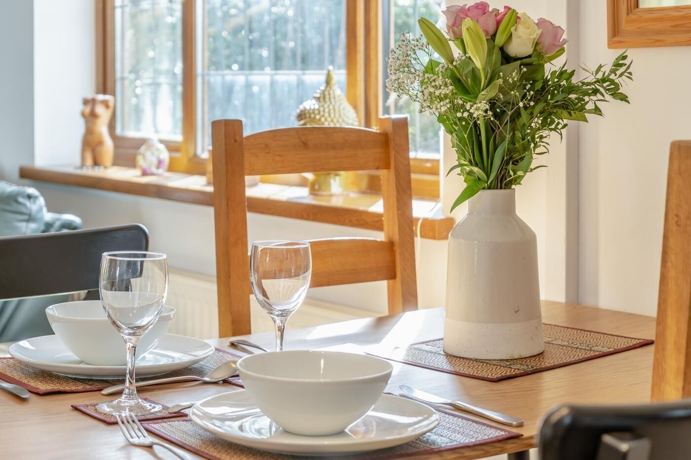 Une table à manger ornée d’un vase de fleurs, une fenêtre donnant sur un beau paysage et une chaise en bois.