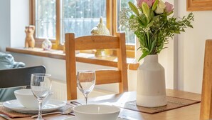 Ein Esstisch mit Blumen in einer Vase, ein Fenster mit Blick und ein Holzhocker.
