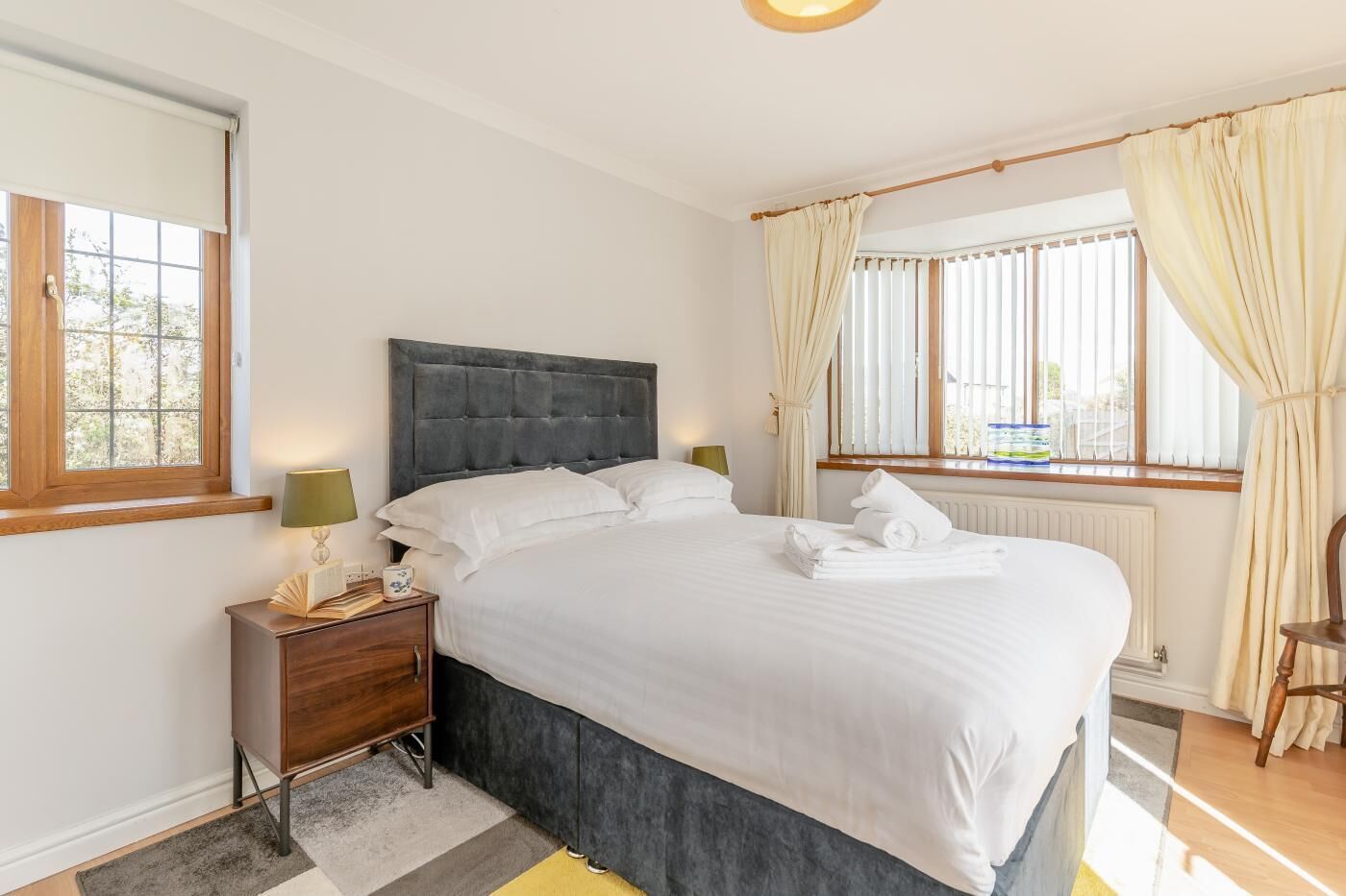A bedroom with a bed, nightstand, lamp, and window with curtains.
