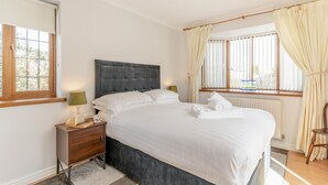 Ein Schlafzimmer mit Bett, Nachttisch, Lampe und einem Fenster mit Vorhängen.