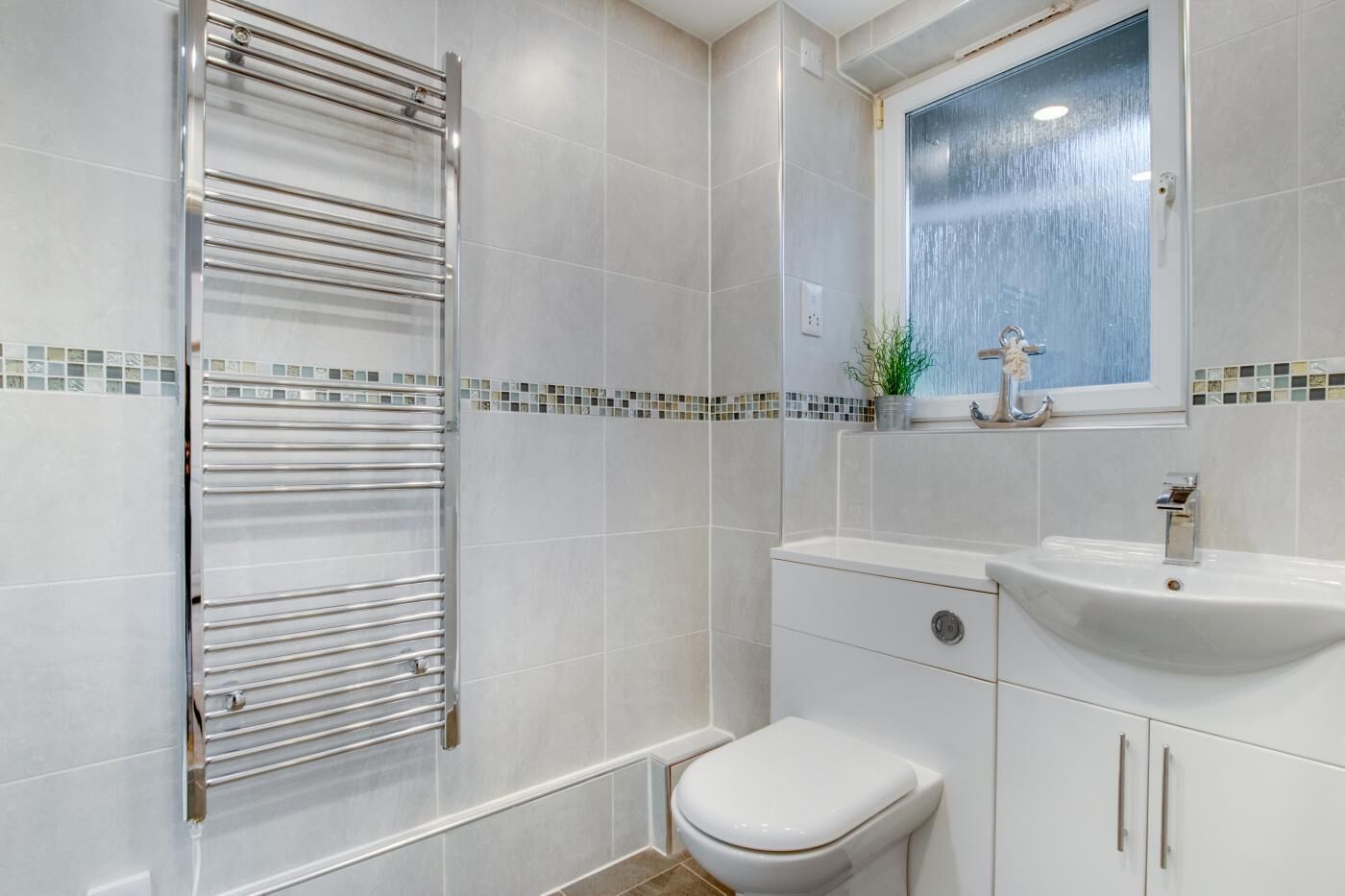 A modern bathroom with a glass shower enclosure, a white toilet, a sink with a mirror, and tiled walls.