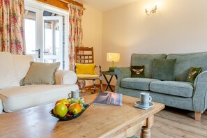 A living room with a sofa, a wooden coffee table with fruits, a chair, a lamp, and a green sofa with decorative pillows.