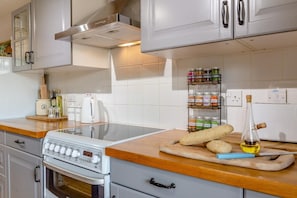 Una cocina con estufa, horno y una encimera con frascos y una botella.