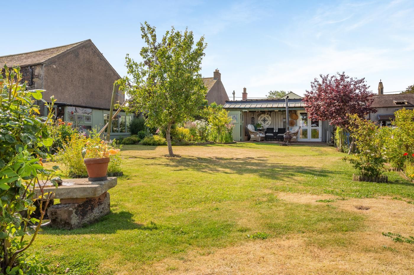 A residential property with a well-maintained lawn, a patio with seating, and a variety of plants.