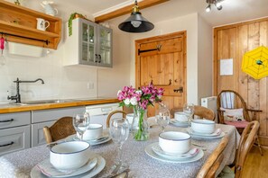 Un comedor con una mesa dispuesta para cuatro personas, rodeada de sillas, un jarrón de flores y una puerta de madera al fondo.
