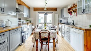 Una cocina moderna con gabinetes grises, encimeras de madera, una mesa de comedor para cuatro personas y una planta colgante.