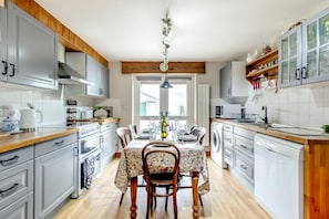 Une cuisine moderne avec des meubles gris, des plans de travail en bois, une table à manger pour quatre personnes et une plante suspendue.
