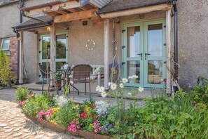 Una casa amb un porxo cobert, una zona de menjador amb cadires i un jardí de flors.