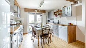 Una cocina moderna con vigas de madera, una mesa de comedor preparada para cuatro personas y vistas a través de la puerta de cristal.
