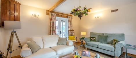 A cozy living room with a white sofa, a green sofa, a wooden coffee table with fruits, and a tripod lamp.