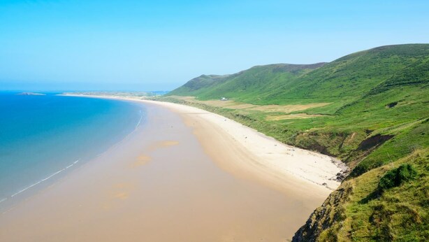 Paesaggio costiero con spiaggia sabbiosa e colline verdi.