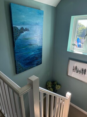 A staircase with white railings, a blue wall with a large abstract painting, and a framed photograph of surfers.