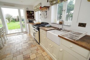 A kitchen with a stone floor, white cabinetry, a gas stove, and a window with a view of the garden.