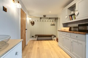 Una cocina con suelo de madera, armarios blancos, una banca y luces fijadas a la pared.