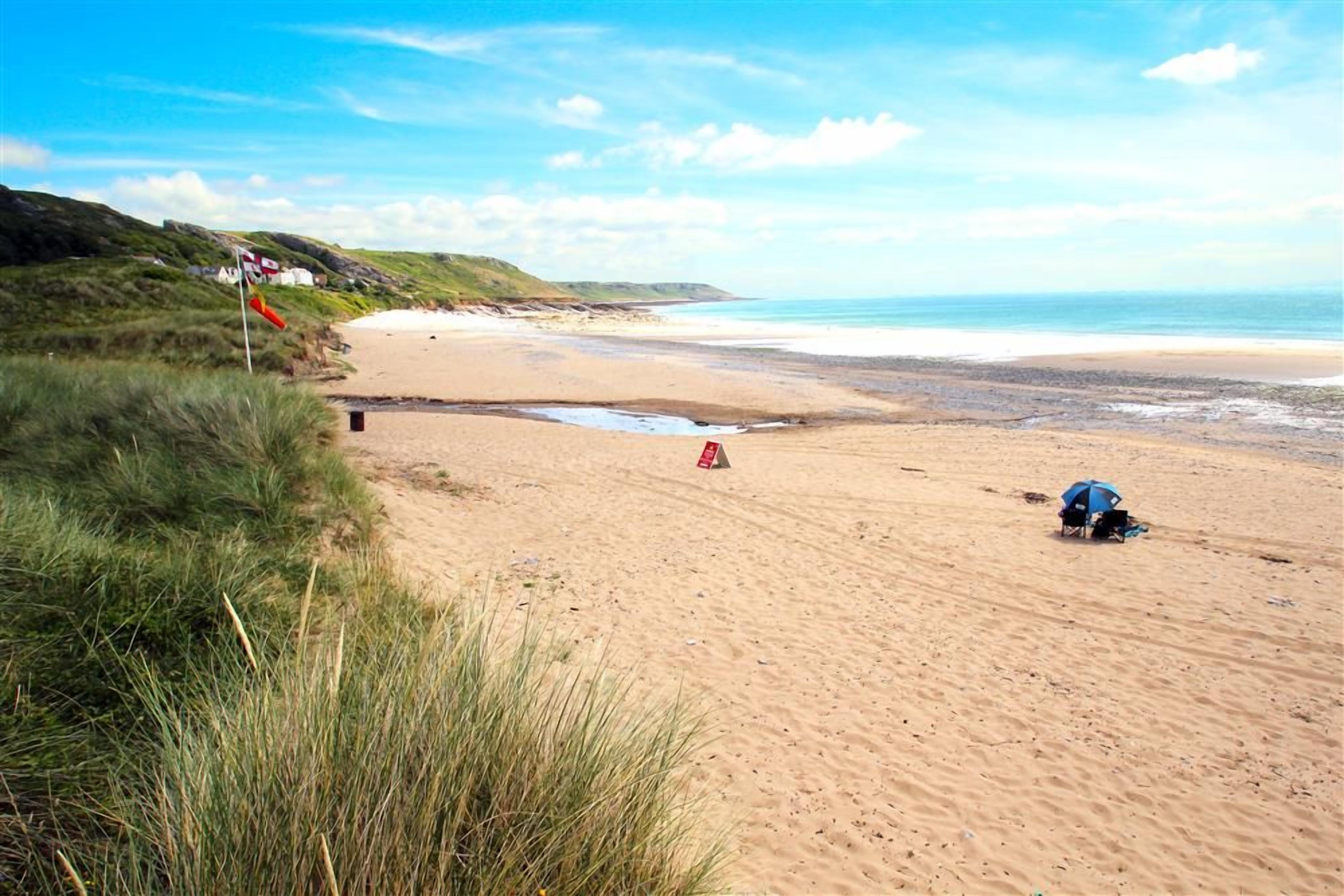 A sandy beach with a blue umbrella and a red flag.