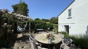 Eine Terrasse mit Korbmöbeln, einem runden Tisch mit Früchten und Getränken sowie einer Pergola mit Kletterpflanzen.