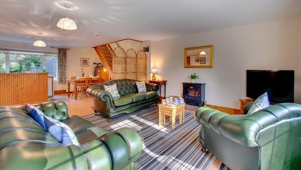 A cozy living room with a green sofa, a striped rug, a fireplace, and a dining area with wooden furniture. - 2 Bed in Felindre (oc-hh39) (Felindre)
