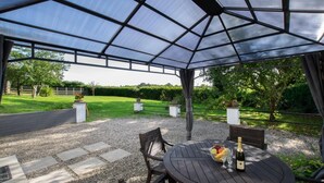 A covered outdoor seating area with a table set for two, a bottle of champagne, and a fruit bowl. - 2 Bed in Felindre (oc-hh39) (Felindre)