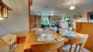 A dining area with a wooden table set for four, surrounded by wicker chairs. A bottle of wine and glasses are on the table. - 2 Bed in Felindre (oc-hh39) (Felindre)