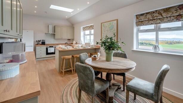 A modern kitchen with a central island, wooden flooring, and a view of the countryside through a window. - 2 Bed in Alyth (oc-e31854) (Auchrannie)