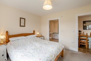 Een slaapkamer met een houten bed, nachtlampjes, een ingelijste foto aan de muur, en een badkamer die door een open deur zichtbaar is.