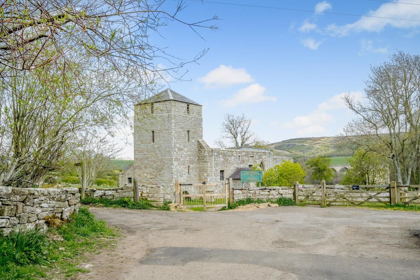 A stone tower with a gate, surrounded by stone walls and greenery.