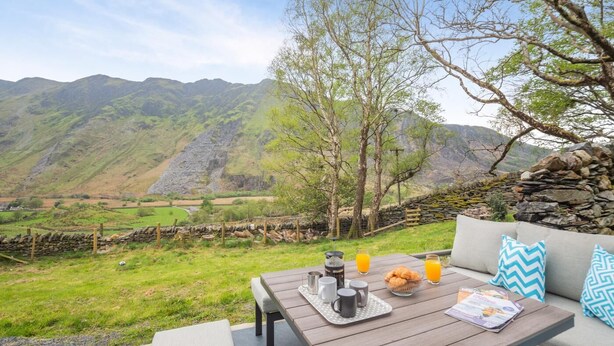 A table set outdoors with a scenic mountain view, a stone wall, and a wooden bench. - 3 Bed in Nant Peris (oc-f31804) (Nant Peris)