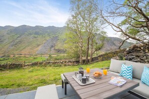 Une table dressée à l’extérieur, offrant une vue pittoresque sur les montagnes, avec un mur en pierre et un banc en bois.