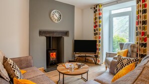 A living room with a fireplace, a television, and a sofa with patterned cushions. - 3 Bed in Nant Peris (oc-f31804) (Nant Peris)