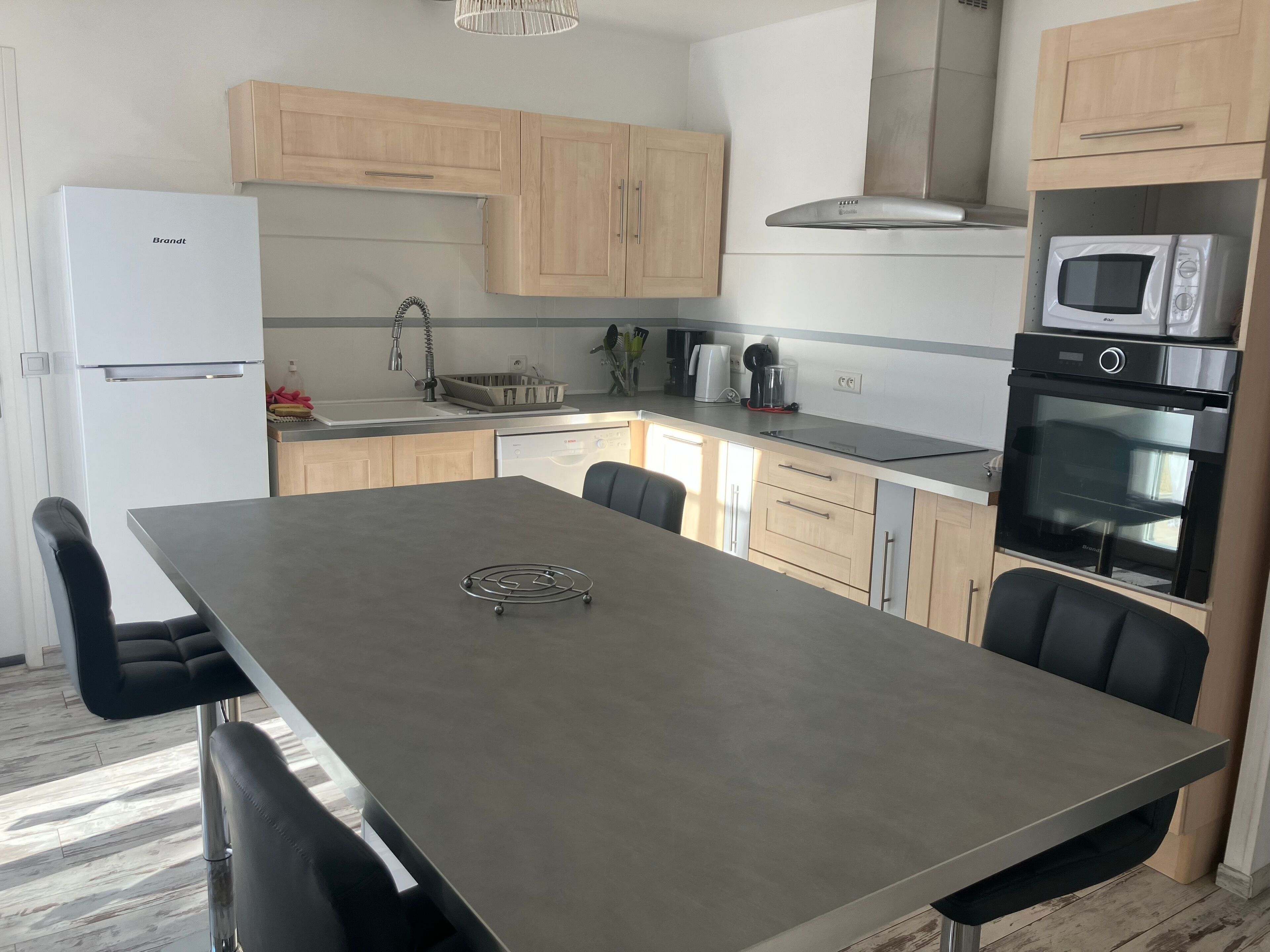 Une cuisine moderne dotée d’un îlot central, d’appareils électroménagers en acier inoxydable et de meubles de rangement en bois clair.