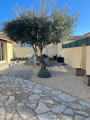 Une cour avec une terrasse en pierre, un arbre, du mobilier d’extérieur et un bâtiment doté d’un toit en tuiles.