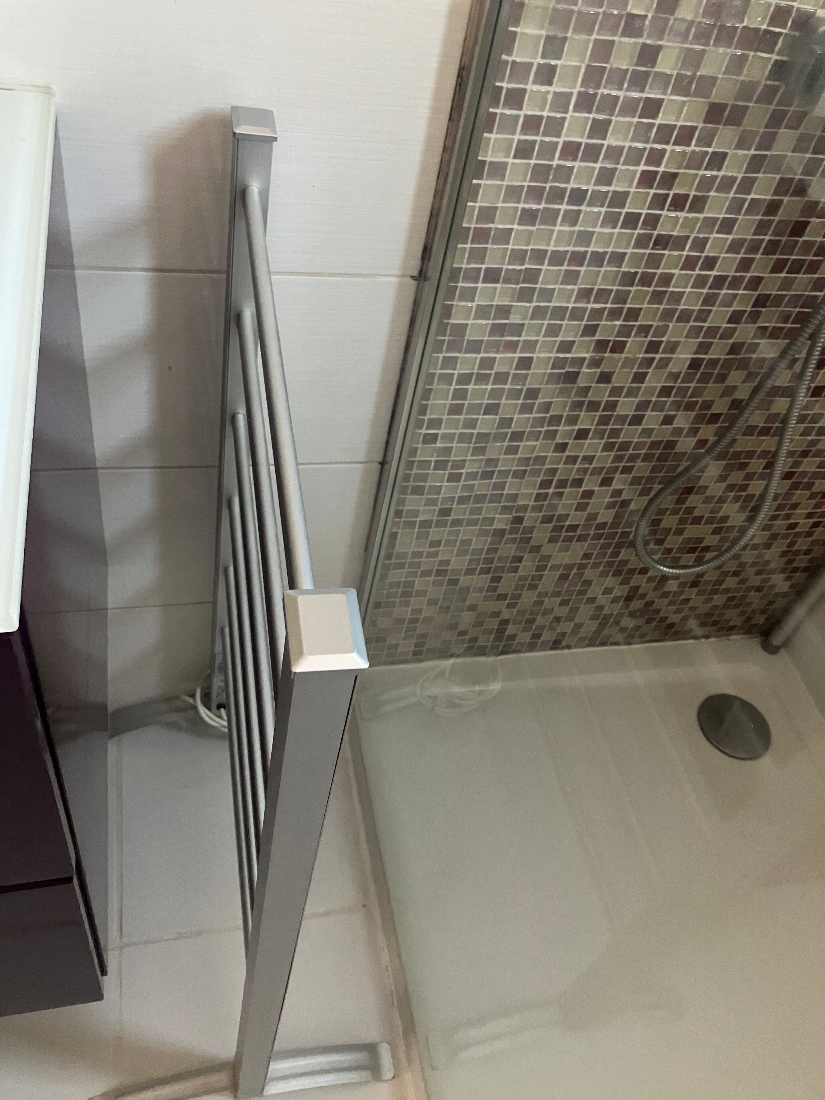 Un espace douche doté d’une porte en verre, d’une poignée en métal et d’un mur carrelé.