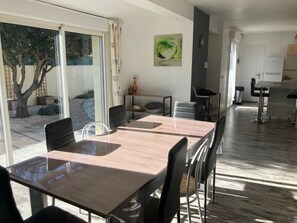 Un comedor amplio con una mesa grande y sillas, una zona de cocina con electrodomésticos modernos, y vistas a un jardín a través de amplios ventanales.