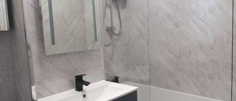A modern bathroom with a white sink, black cabinets, a glass shower enclosure, and a white bathtub.