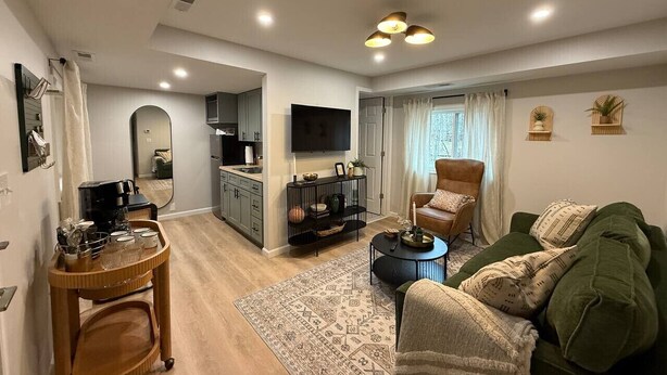 A modern living room with a sofa, coffee table, and a TV. There's a kitchen area with cabinets and a dining table.