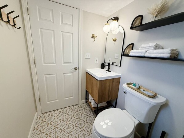 Une salle de bain avec une porte blanche, un meuble-lavabo en bois, des toilettes blanches et une étagère avec des serviettes.