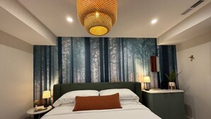 A bedroom with a large bed, a nightstand with a lamp, a wall-mounted shelf, and a forest-themed wallpaper.