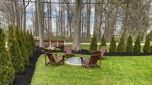 A well-maintained outdoor seating area with a circular fire pit, surrounded by neatly trimmed hedges and a variety of trees.