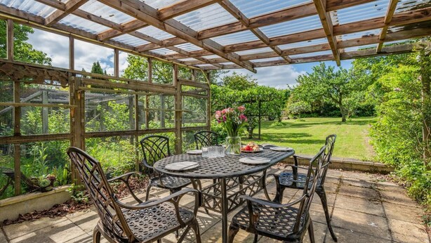 Eine überdachte Terrasse mit rundem Tisch und Stühlen, umgeben von einer Holzpergola und einer Glasveranda.