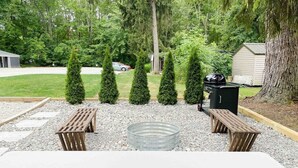 A patio with a white table, two wooden benches, a metal fire pit, and a barbecue grill. - Endless Summer Cottage - walk to the GOTL strip (Geneva)