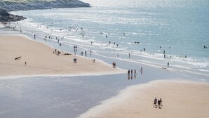 Ein weiter Sandstrand mit Menschen, die spazieren gehen und schwimmen.