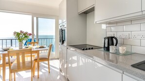 Eine moderne Küche mit großem Fenster zum Meer, ein Essbereich mit Tisch und Stühlen sowie Blick auf den Ozean.